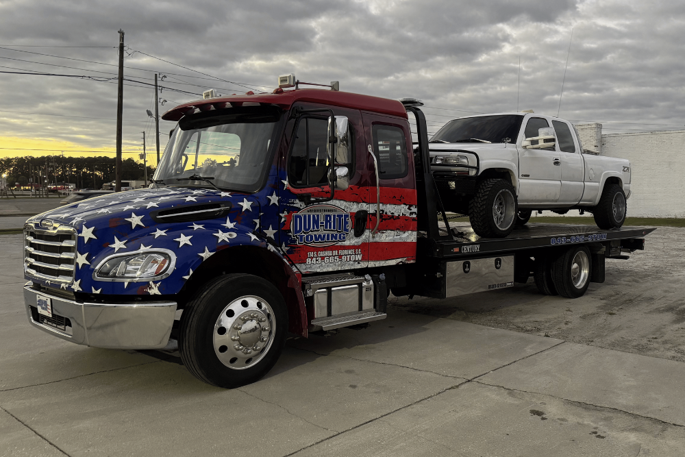Flatbed vs. Wrecker Towing in Florence, SC At Dun Rite Towing. American flag themed flatbed tow truck carrying a white pickup truck
